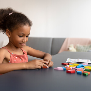 A young girl joyfully plays with a variety of colorful building blocks on a soft surface.