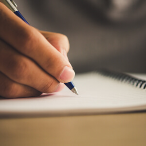 A person diligently writes in a notebook using a pen, illustrating the act of note-taking or journaling.