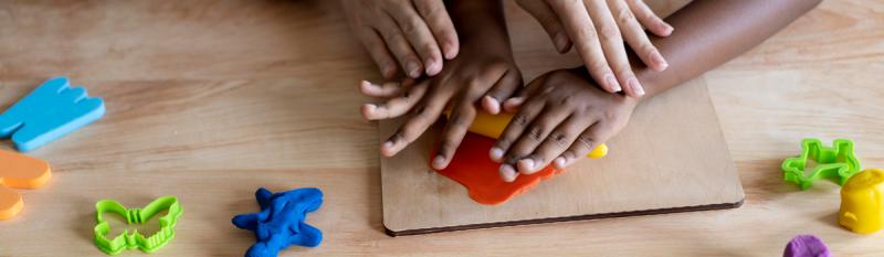 A child's hands grasp a wooden board adorned with various colorful toys, showcasing playful engagement and creativity.