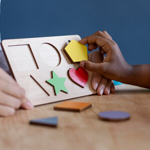 A child focused on assembling a colourful wooden puzzle on a table, showcasing engagement and cognitive development.