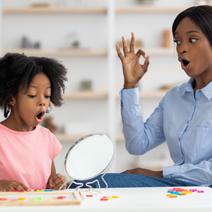 A woman and a little girl are seated at a table, looking into a mirror, engaged in a shared experience.