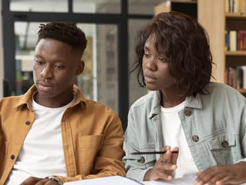 Two students engaged in studying together at a library table, surrounded by books and notes.