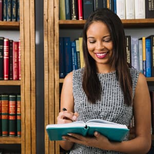 A cheerful woman smiles while holding a book, radiating happiness and engagement with her reading material.