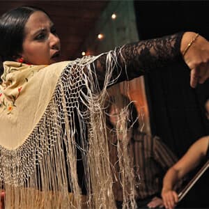 A woman in a fringed dress stands in front of the camera, pointing.
