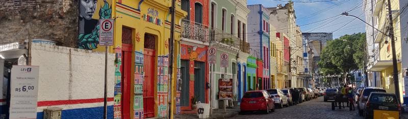 A narrow street lined with vibrant buildings and parked cars, showcasing a lively urban atmosphere.