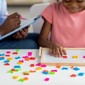A child and her teacher collaboratively assembling a colourful puzzle on a table, focused and engaged in the activity.