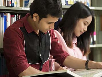 Two students engaged in studying together at a library table, surrounded by books and notes.