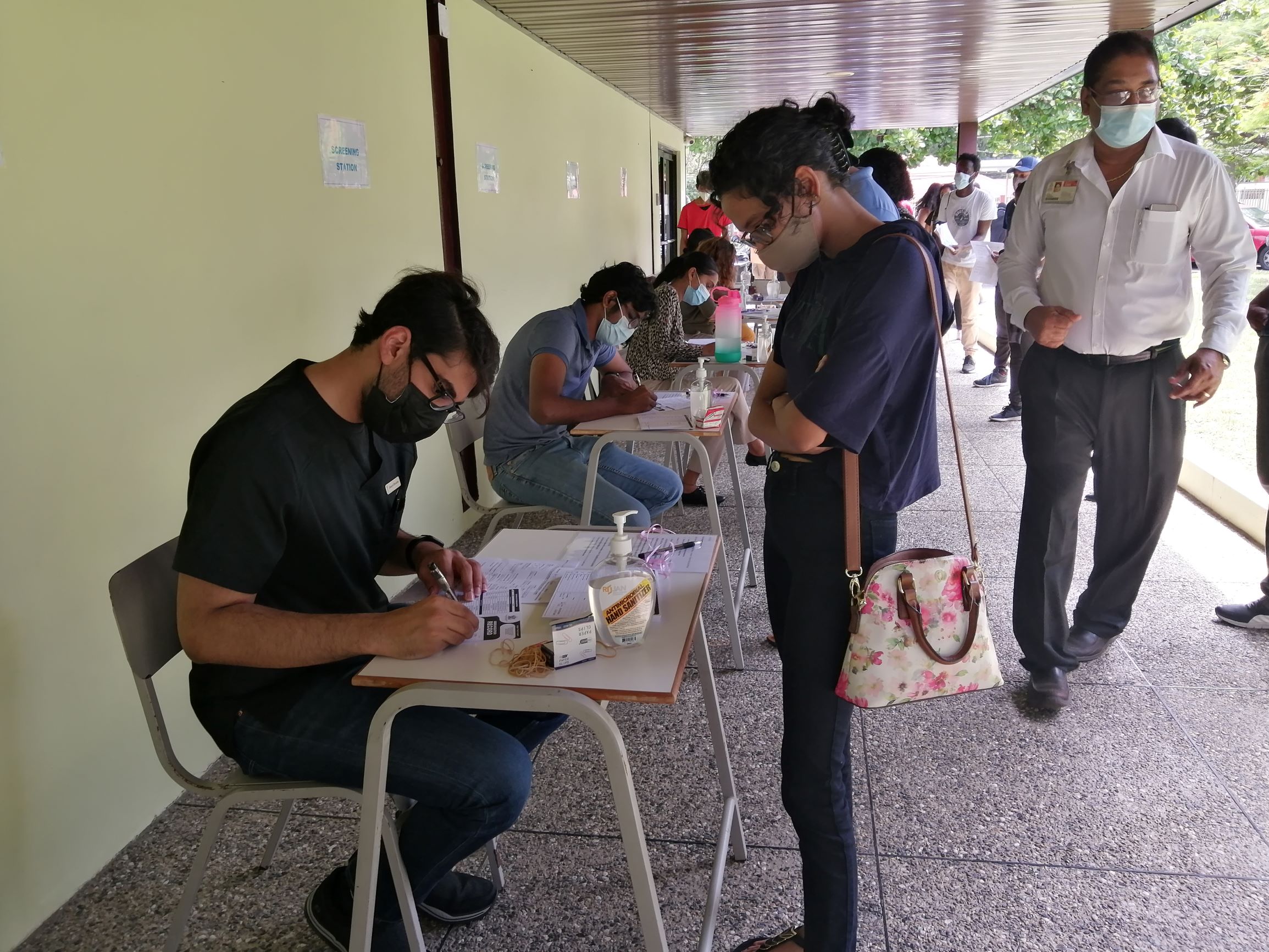 A UWI St. Augustine Campus student gets her documents checked by a UWI student volunteer before being administered the COVID-19 vaccine at The UWI Inn and Conference Centre. At right supervising the exercise is Dr. Neil Singh, Head, Health Services Unit The UWI St. Augustine Campus